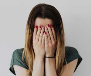 White lady in grey top with hands covering face sadly