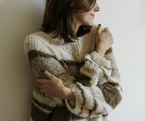 Lady huggin self in cosy jumper and looking off to the right